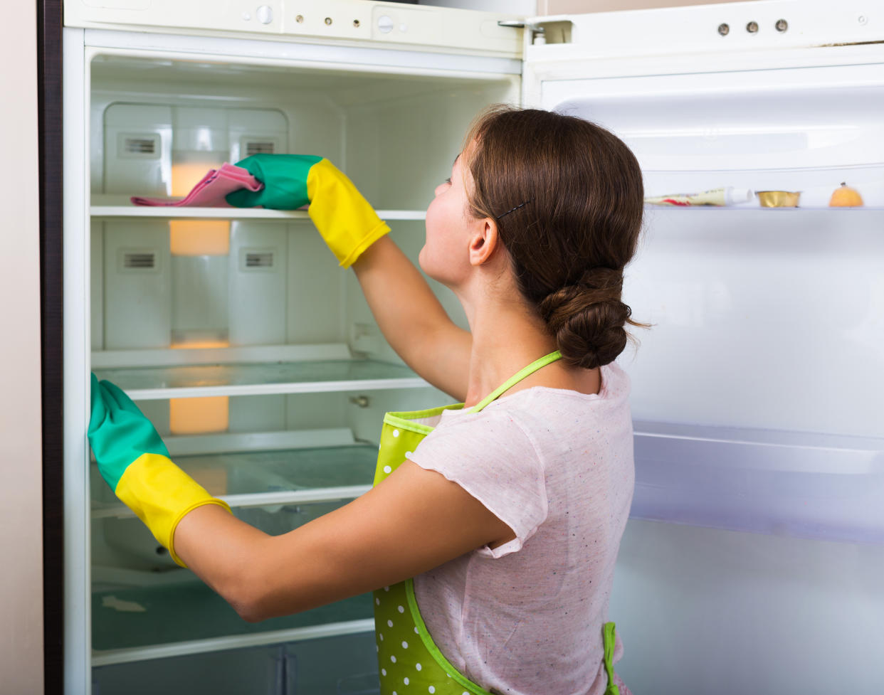 Adult housewife cleaning refrigerator inside and smiling