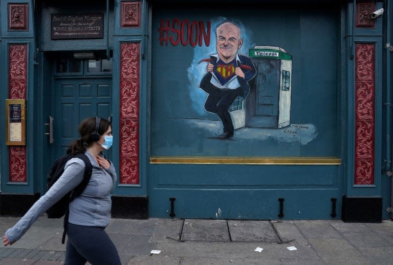 FILE PHOTO: A woman wearing a protective face mask walks past artwork depicting Tony Holohan Chief Medical Officer for the Irish Department of Health painted on the shuttered windows of a pub following the outbreak of the coronavirus disease (COVID-19), in Dublin, Ireland, May 15, 2020. REUTERS/Clodagh Kilcoyne/File Photo