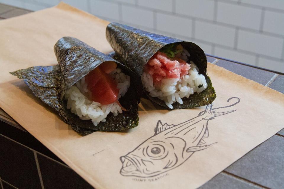 A photo of two hand rolls, lean tuna and fatty tuna, on the counter atop brown paper featuring a sketch of a fish.