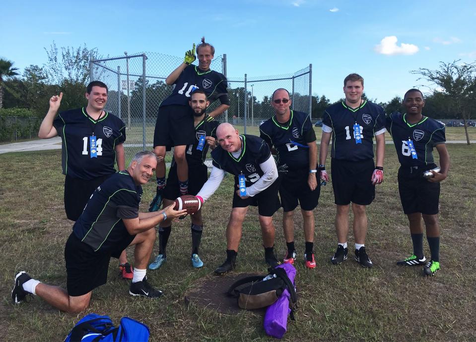 Coach Chris Schaier (left, kneeling) and son Fletcher (second from right) pose with their North Florida School of Special Education flag football team after winning first place in an area tournament in 2018. The elder Schaier and two other men — Luis Mangual (#1) and Dan Mcaulif (#49) — are "unified partners," meaning they coach and play alongside intellectually disabled team members. The other players are Ryan Smith (#14), Alek Drysdale (#10), Jonathan Dutton (#2), Fletcher Schaier (#12) and Nolan White (#6).