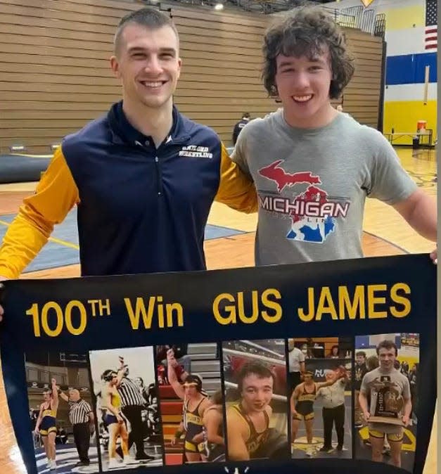 Gus James (right) and coach Dan Cornish (left) pose with a banner celebrating James's 100th career win as a Gaylord Wrestler on Wednesday, January 18.