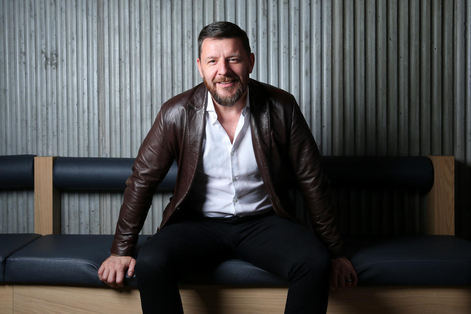 My Kitchen Rules' Manu Feildel sits on a bench at the official opening of Henrietta, wearing a brown leather jacket over an unbuttoned white shirt