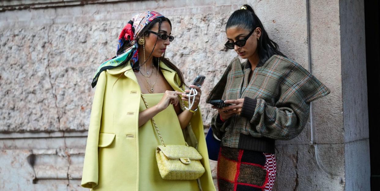 milan, italy september 21 melanie darmon r wears a gold hair clip, black sunglasses, gold earrings, a brown with blue and red checkered print pattern oversized jacket, a red black white embroidered wool pattern knees skirt, gabriella berdugo l wears a red blue white print pattern silk scarf on the head, black sunglasses, silver earrings, gold necklaces, a yellow shoulder off short dress, a pale yellow jacket, a pale yellow and white tweed crossbody bag from chanel, outside alberta ferretti, during the milan fashion week womenswear springsummer 2023 on september 21, 2022 in milan, italy photo by edward berthelotgetty images