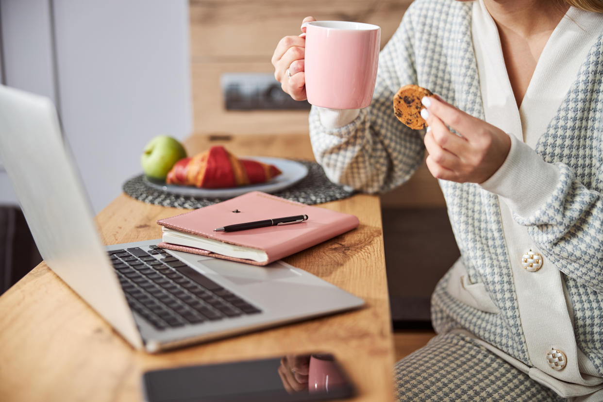 Person having a snack of biscuits with chocolate crumbs and tea while sitting in front of laptop