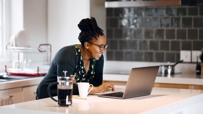 Shot of a smiling young woman using laptop on kitchen counter.