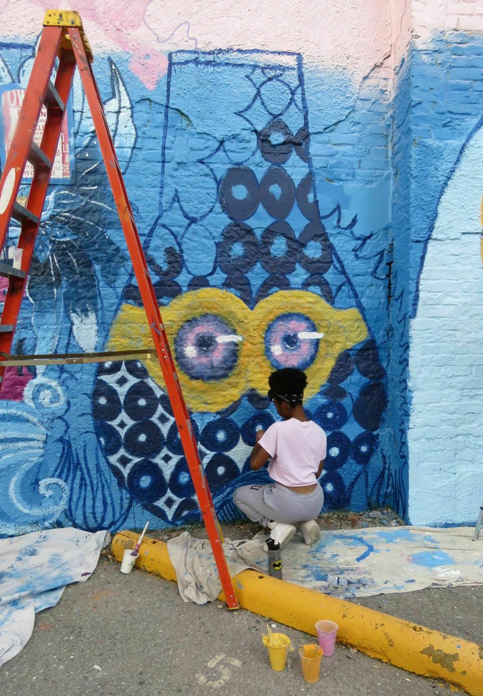 In this Thursday, May 30, 2019 photo, Shanti Broom works on a detail of the gorud-shaped fish she created as the capital letter I in the word "SURVIVE" for a mural by Brandon "BMike" Odoms and students from the Young Artist Movement in downtown New Orleans. The mural is one of five created as part of an Arts Council of New Orleans project called "Unframed." The council's executive director, Heidi Schmalbach, says the group wants New Orleans to be known for its contemporary art as much as for its music, food and culture. (AP Photo/Janet McConnaughey)