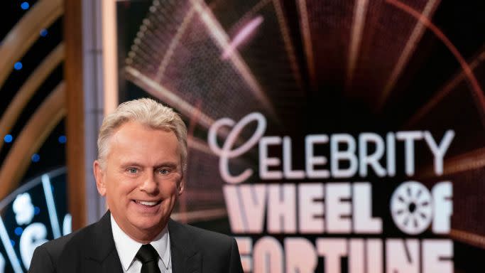 pat sajak smiling for a photo in front of the wheel of fortune logo