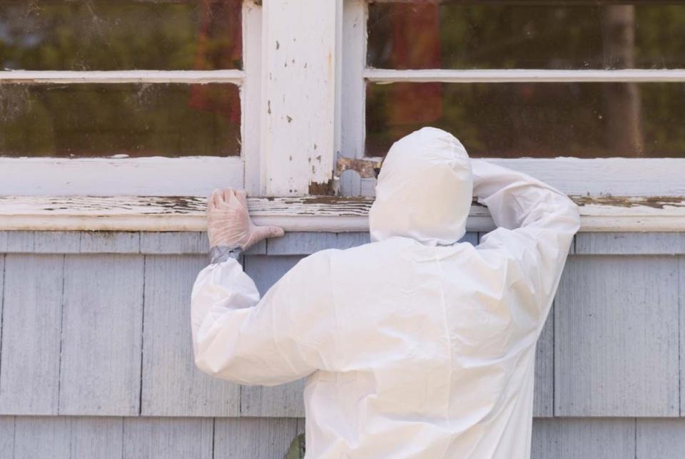 Professional in white tyvek suit removing lead-based paint.