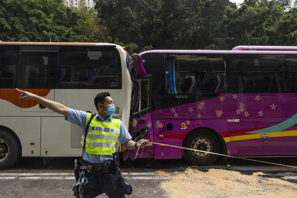 A police officer inspects after an accident on a highway in Hong Kong, Friday, March 24, 2023. Four passenger buses and a truck collided near a Hong Kong road tunnel Friday, injuring dozens of people. (AP Photo/Louise Delmotte)