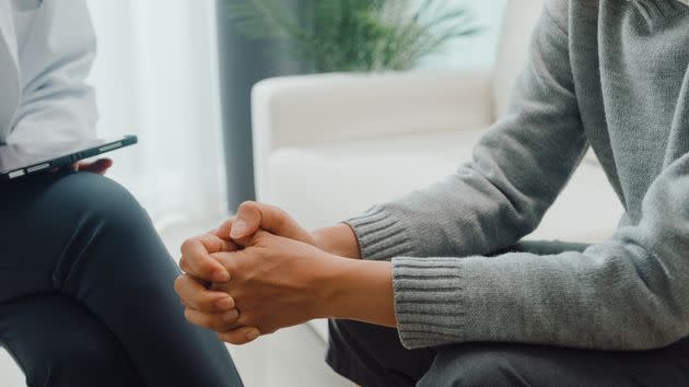 Closeup of young Asian female psychotherapist discussing a problem and touch hand young depressed sit on couch at clinic. Medical insurance, Mental health concept.