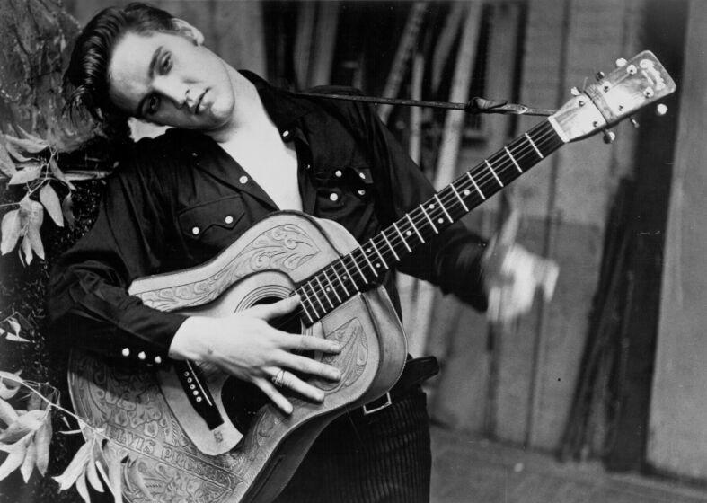 Rock and roll singer Elvis Presley poses for a portrait holding an acoustic guitar in 1956