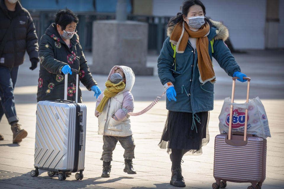 Travelers wear face masks as they walk outside the Beijing Railway Station in Beijing, Saturday, Feb. 15, 2020. People returning to Beijing will now have to isolate themselves either at home or in a concentrated area for medical observation, said a notice from the Chinese capital's prevention and control work group published by state media late Friday. (AP Photo/Mark Schiefelbein)