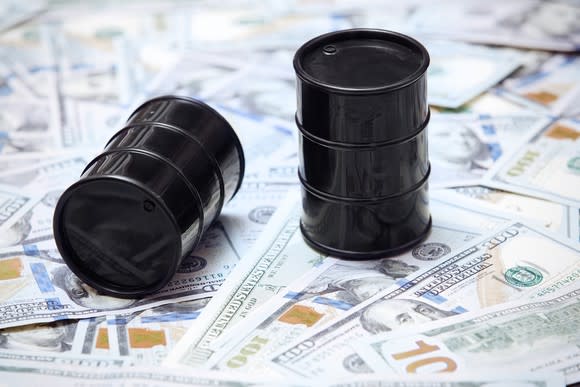 Two plastic oil barrels on top of a pile of U.S. paper money