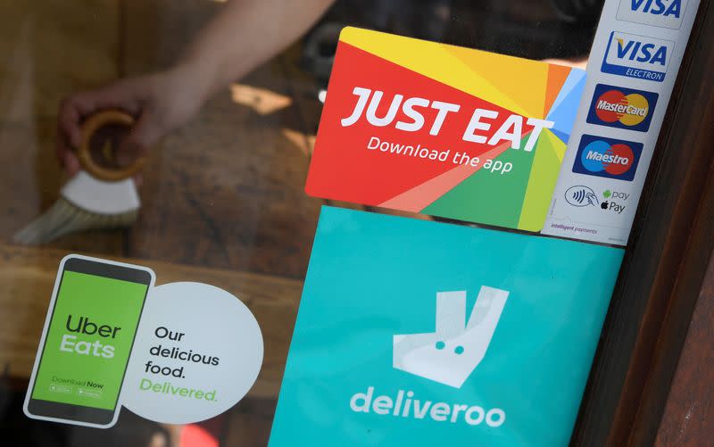 FILE PHOTO: Signage for Just Eat is seen next to Uber Eats and Deliveroo advertisements on the window of a restaurant in London