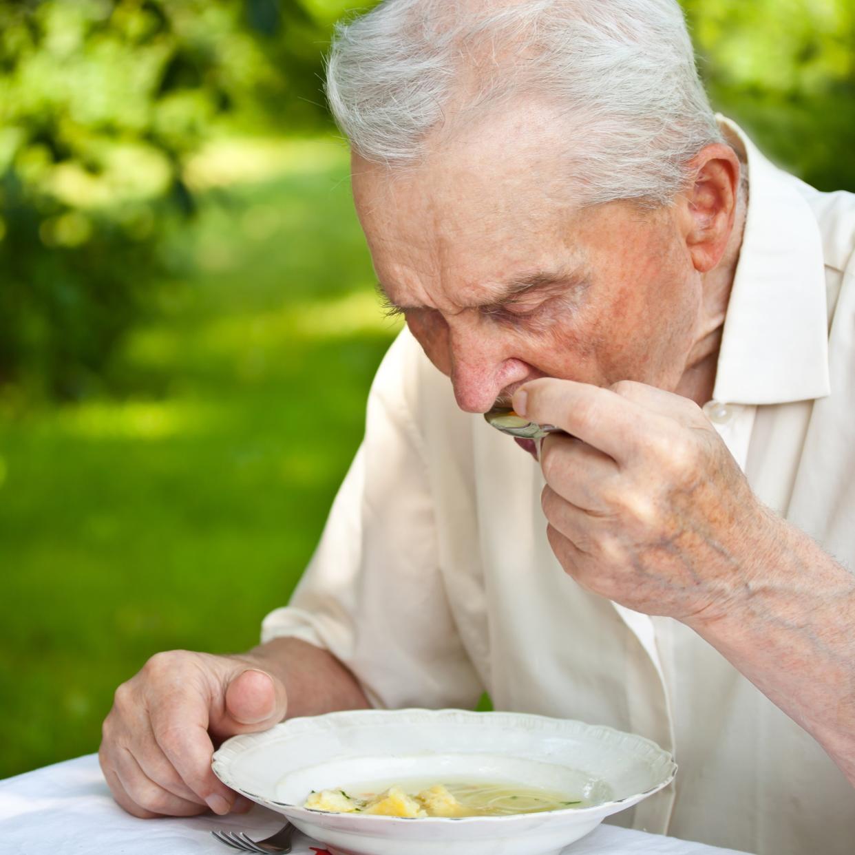 senior man eating a soup outdoors