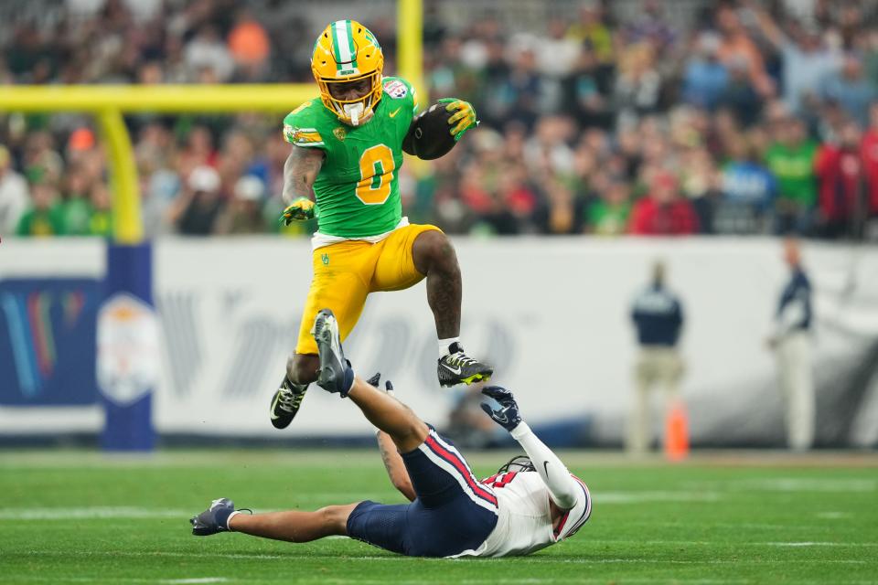 Oregon Ducks running back Bucky Irving (0) hurdles over Liberty Flames defensive back Brandon Bishop (6) during the second half in the 2024 Fiesta Bowl at State Farm Stadium.