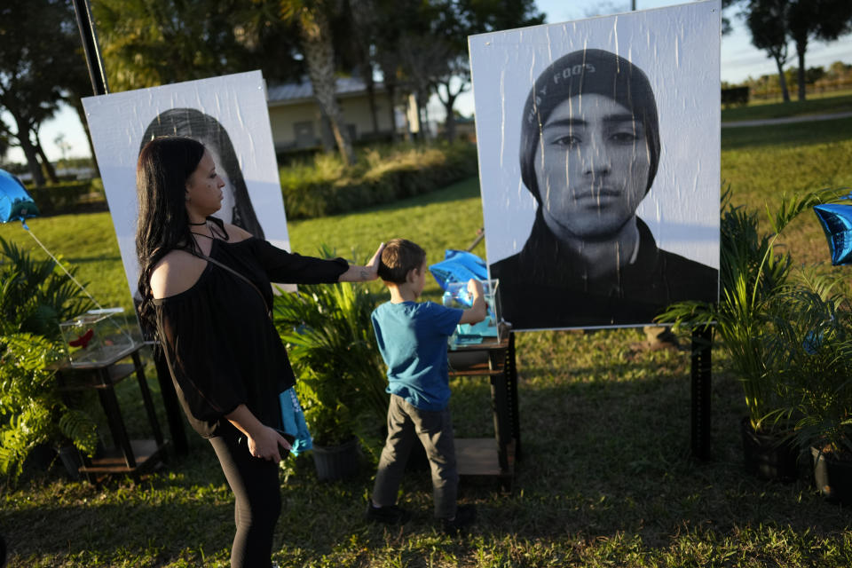 Mariana Rocha and her son Jackson Laparl, 6, visit a portrait of Rocha's cousin Joaquin Oliver, part of a display of portraits of the 17 students and staff of Marjory Stoneman Douglas High School who were killed, during a community commemoration on the five-year anniversary of the shooting, Tuesday, Feb. 14, 2023, at Pine Trails Park in Parkland, Fla. Family members, neighbors and well wishers turned out to multiple events Tuesday to honor the lives of those killed on Valentine's Day 2018. (AP Photo/Rebecca Blackwell)