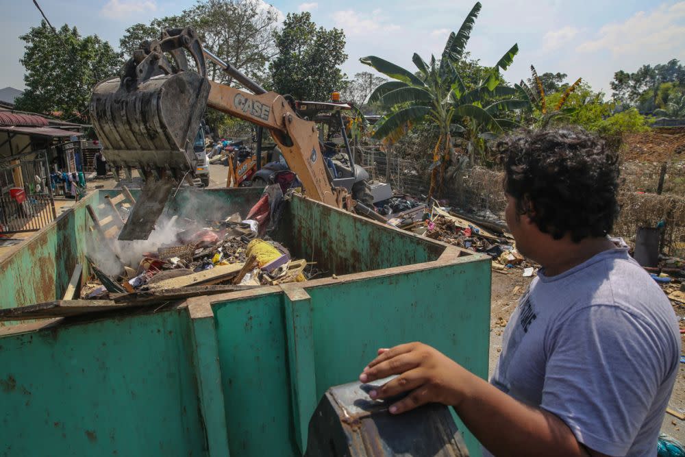 A man looks on as an excavator clears debris and rubbish off the streets in Taman Sri Muda, Shah Alam December 29, 2021. — Picture by Yusof Mat Isa