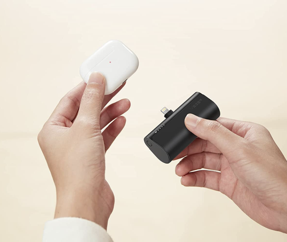 hands holding airpods and black Mini Portable Phone Charger (Photo via Amazon)