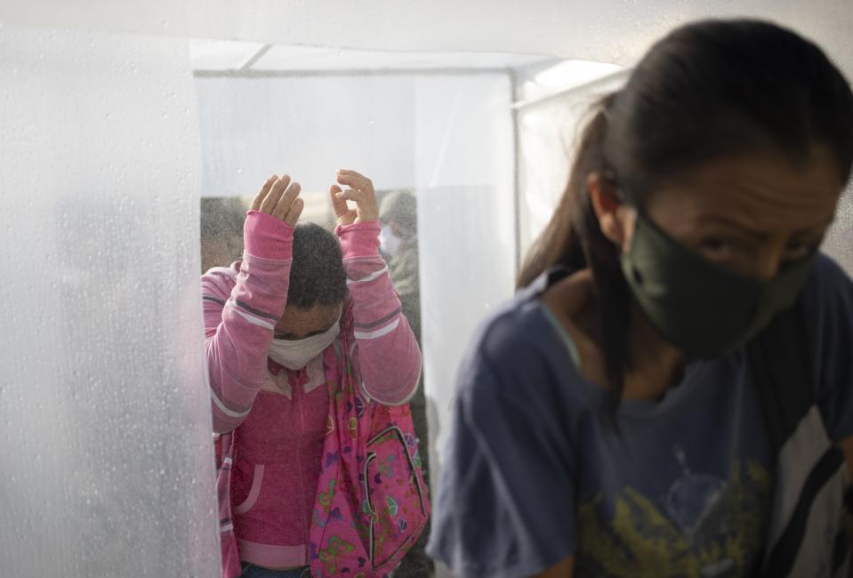 People wearing protective face masks walk through a decontamination chamber as a preventive measure against the spread of the new coronavirus, before entering a popular market in Caracas, Venezuela, March 18, 2020. (AP Photo/Ariana Cubillos)