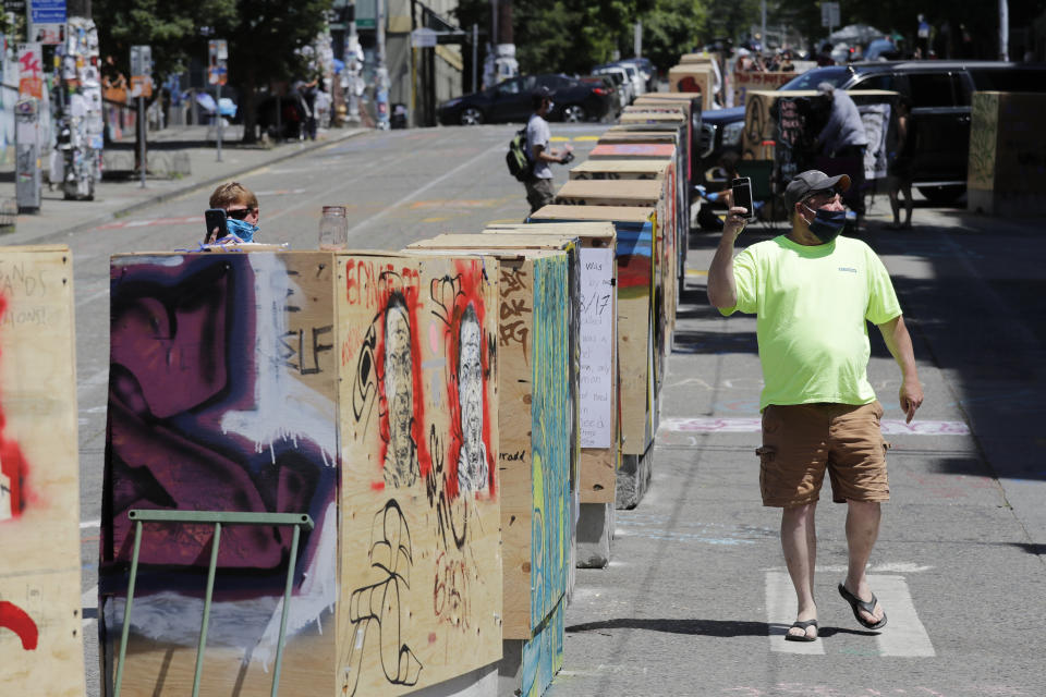 A man walks past barricades blocking a street adjacent to a closed Seattle police precinct Thursday, June 18, 2020, in Seattle, in what has been named the Capitol Hill Occupied Protest zone. Police pulled back from several blocks of the city's Capitol Hill neighborhood near the police department's East Precinct building earlier in the month after clashes with people protesting the death of George Floyd in Minneapolis. (AP Photo/Elaine Thompson)