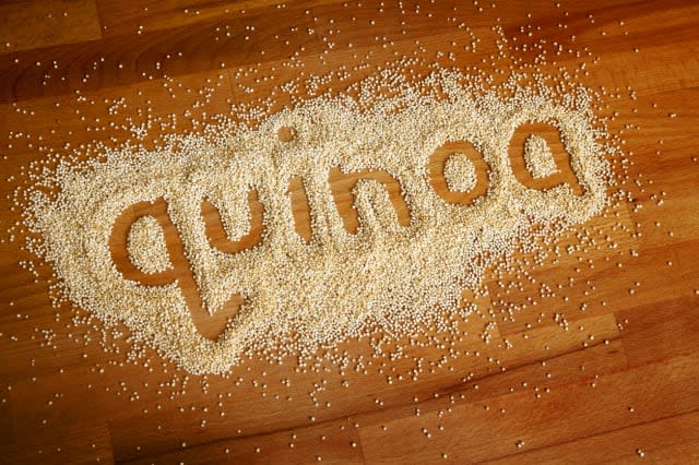 The word 'quinoa' written by finger in some quinoa sprinkled over a kitchen's wooden worktop.