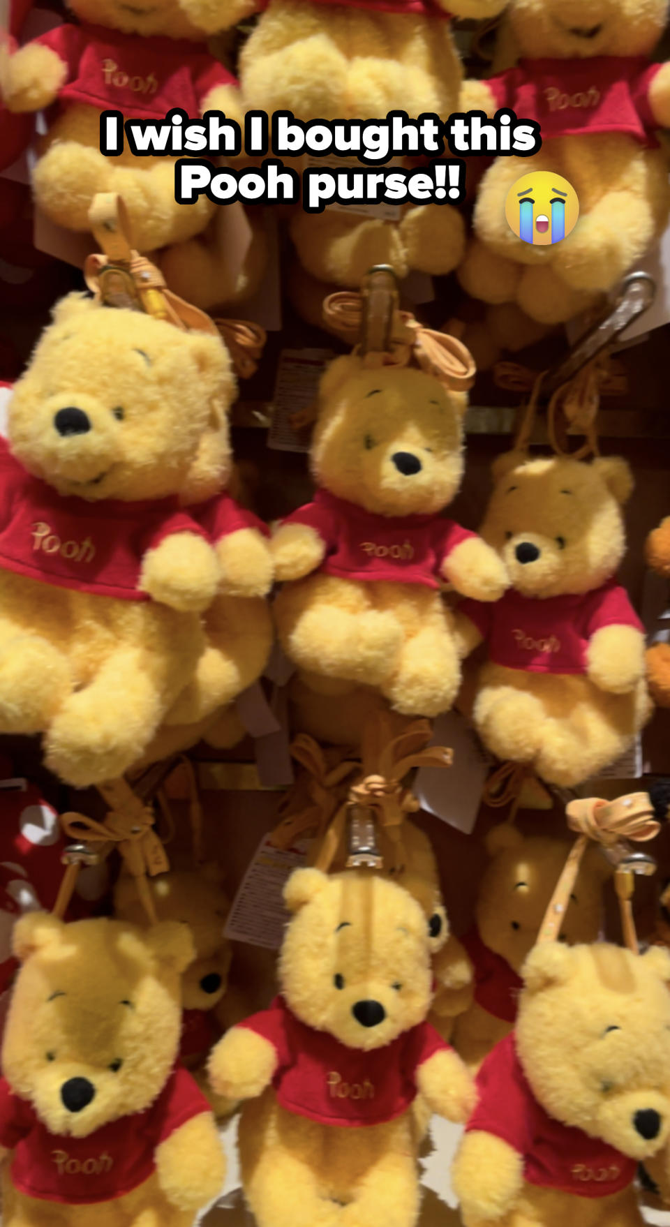 Plush toys of Winnie the Pooh wearing red shirts are displayed in multiple rows on a shelf