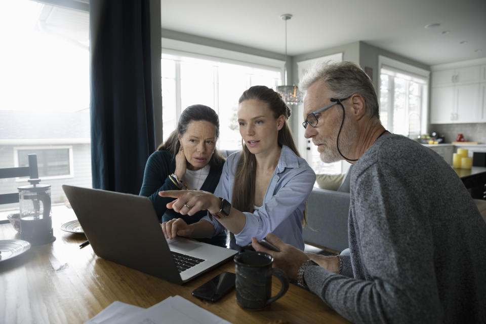 Parents and adult daughter using laptop at dining table