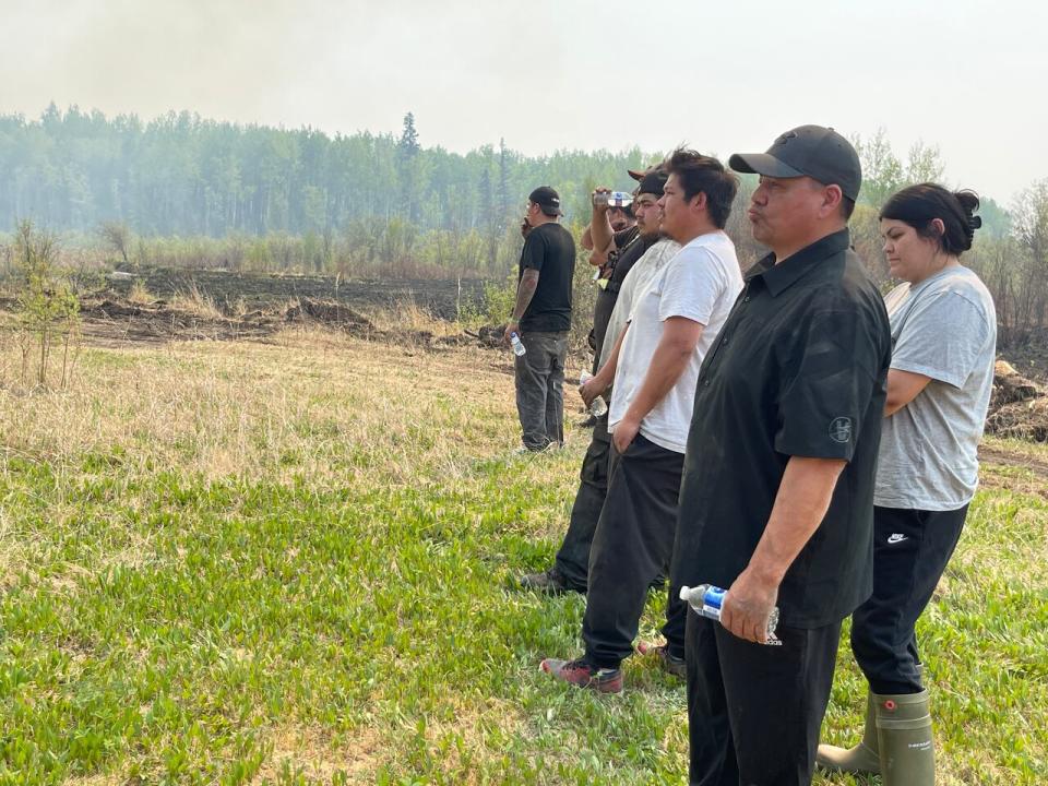 Raymond Supernault, front, stands with other people from the East Prairie Métis Settlement in a field, watching a control burn in 2023.
