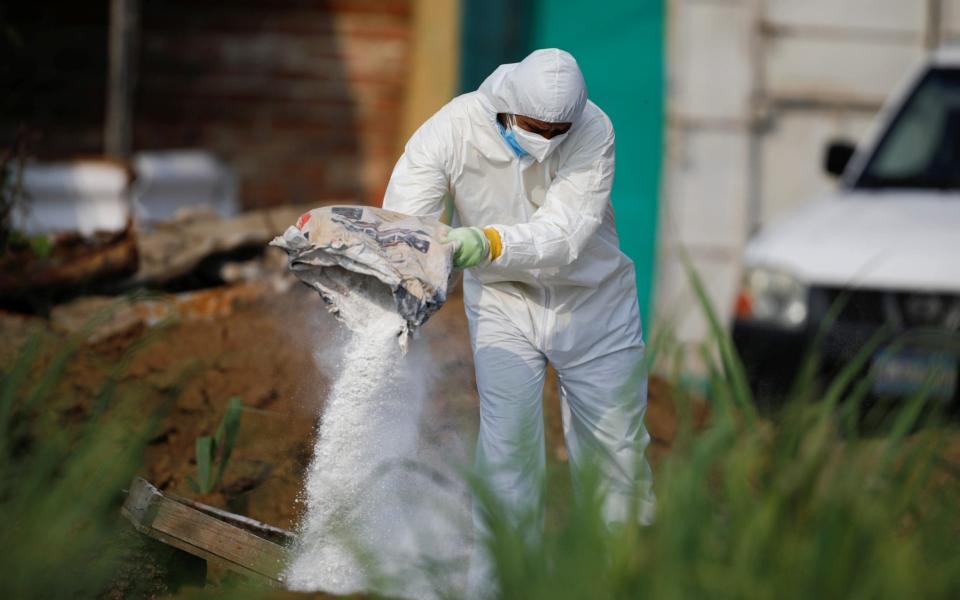 A forensic expert throws lime on discarded protective equipment used where authorities are excavating a clandestine cemetery discovered at the house of a former police officer and containing as many as 40 bodies, most of them believed to be women, in Chalchuapa, El Salvador May 20, 2021 - JOSE CABEZAS /REUTERS