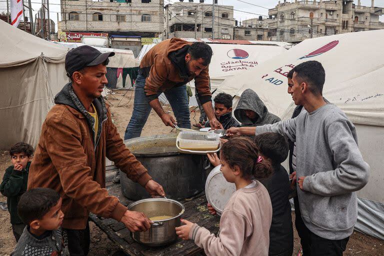 Voluntarios distribuyen raciones de sopa de lentejas rojas a los palestinos desplazados en Rafah, en el sur de la Franja de Gaza, el 18 de febrero de 2024, en medio del conflicto continuo entre Israel y el grupo militante Hamas.