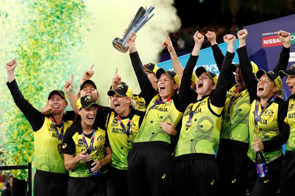 Meg Lanning holds aloft the 2020 T20 championship trophy at the MCG surrounded by her teammates and green and yellow confetti