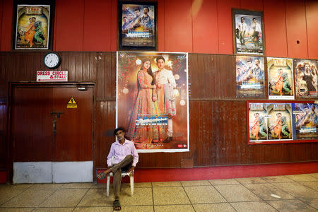 Ticket checker Mukesh, 40, sits by a wall decorated with film posters at the hall of the Bambino Cinema in Karachi, Pakistan August 30, 2018. REUTERS/Akhtar Soomro