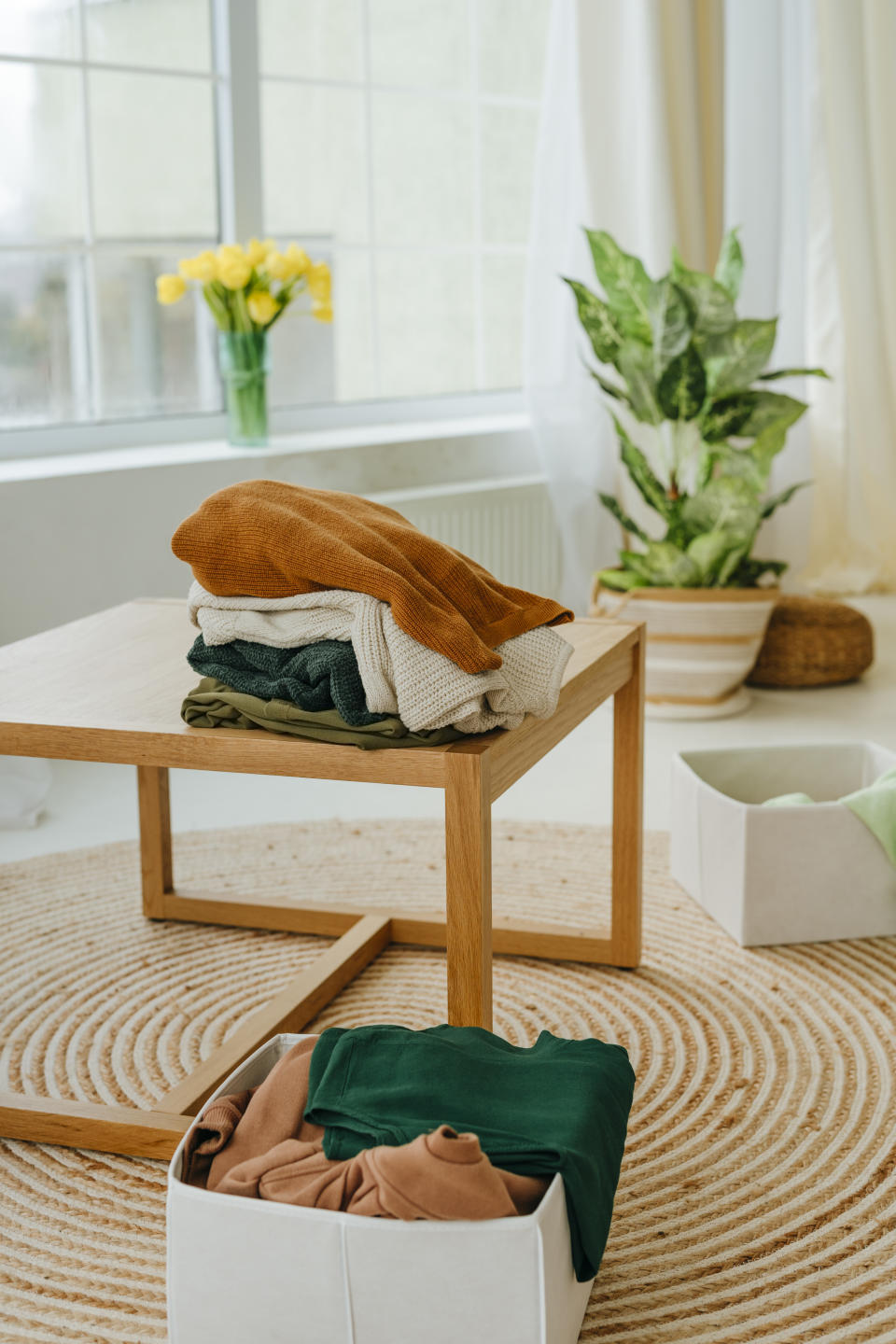 A pile of clothes in a box and another pile placed neatly on a table