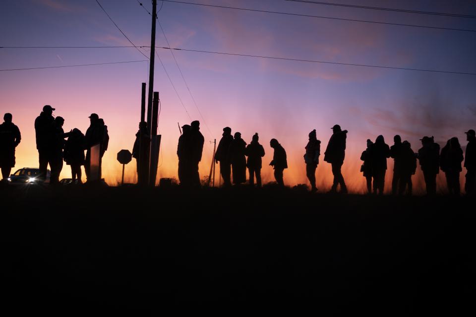 Trump supporters are silhouetted against the setting sun as they wait to board shuttle buses to his rally, Monday, Nov. 2, 2020, in Kenosha, Wis. Trump has made Wisconsin a focus of his final push, including a stop planned Monday night in Kenosha, while repeatedly refusing to say whether he would agree to a peaceful transfer of power if he loses. (AP Photo/Wong Maye-E)