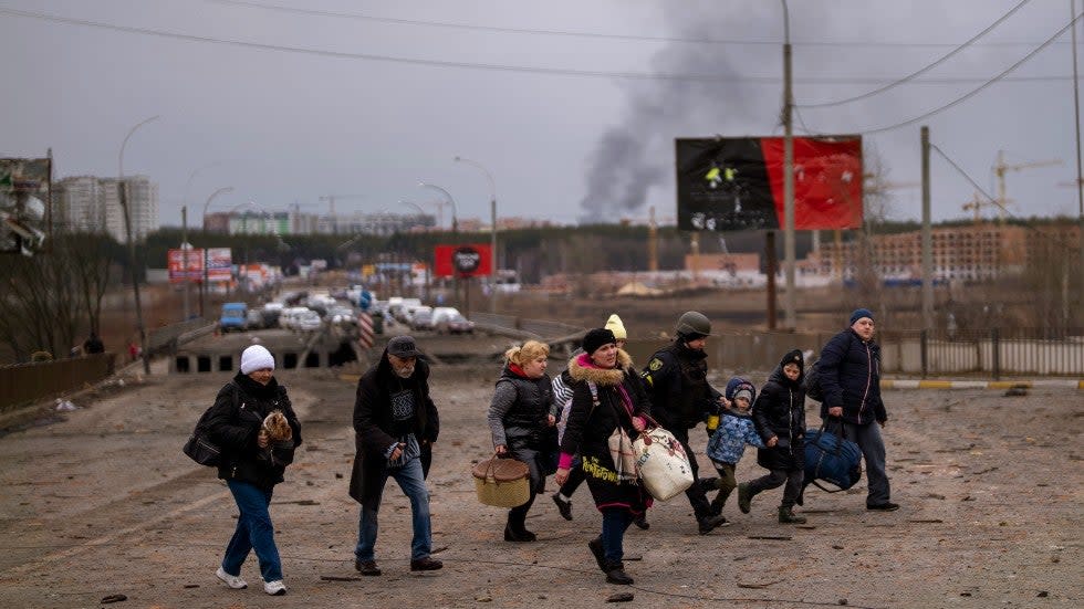 A Ukrainian police officer helps people as artillery echoes nearby while fleeing Irpin in the outskirts of Kyiv