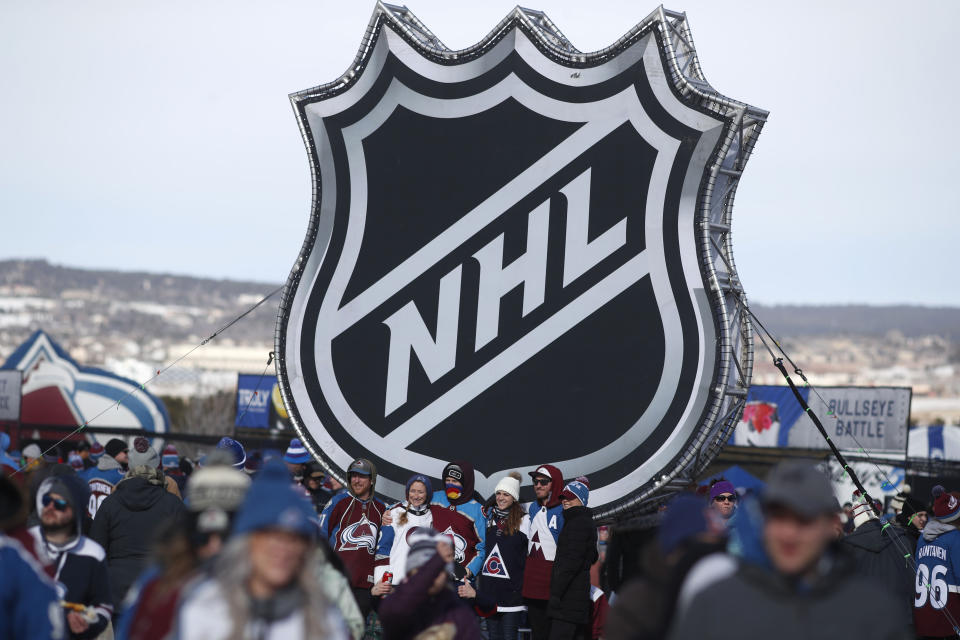 Fans pose below the NHL league logo at a display outside Falcon Stadium before an NHL Stadium Series outdoor hockey game between the Los Angeles Kings and Colorado Avalanche, Saturday, Feb. 15, 2020, at Air Force Academy, Colo. (AP Photo/David Zalubowski)