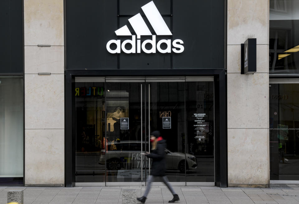 Eine Frau läuft an einem geschlossenen Geschäft des Sportartikelherstellers Adidas entlang. Foto: Axel Heimken / dpa +++ dpa-Bildfunk +++