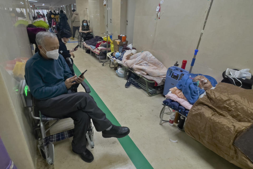 People wearing face masks browse their phones as they look after their elderly relatives rest along a corridor of the emergency ward to receive intravenous drips at a hospital in Beijing, Thursday, Jan. 5, 2023. Patients, most of them elderly, are lying on stretchers in hallways and taking oxygen while sitting in wheelchairs as COVID-19 surges in China's capital Beijing. (AP Photo/Andy Wong)