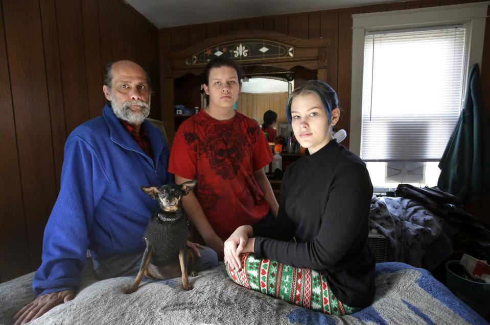 In this Sunday, Dec. 11, 2016 photo U.S. Navy veteran Stephen Matthews, 55, sits for a photograph with his son Alexander, center, and daughter Victoria, right, in the bedroom of a relatives home, in Warwick, R.I. Matthews fell in his driveway in 2015, injuring his neck resulting in him getting laid off from his job. After being evicted he and his wife temporarily lived in their car while his children went to live with a relative. The relative then let Matthews and his wife come too. Matthews said he received a voucher that would pay about two-thirds of his rent, but struggled to find an apartment in Rhode Island where he could afford the balance. He got one in West Warwick, R.I. in late December 2016 after a six-month search. (AP Photo/Steven Senne)