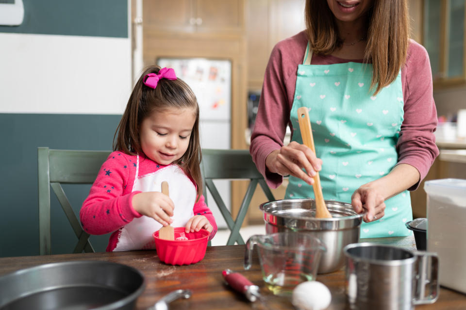 Pretty little girl wearing and apron and getting ready to bake some cookies with her mom in the kitchen