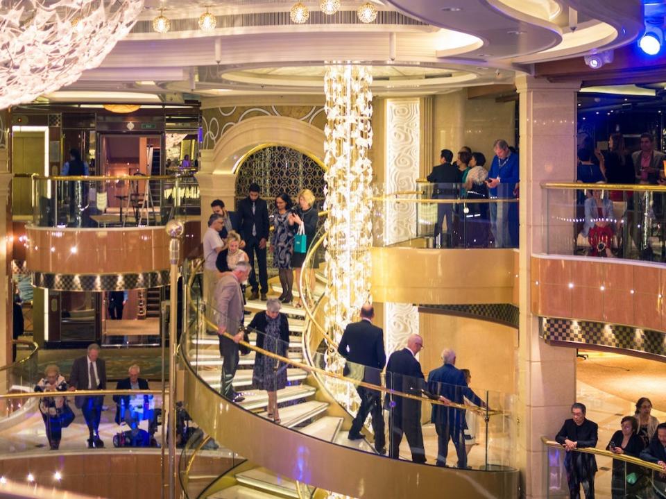 Cruise passengers descend a grand stairwell in formal attire during an evening at sea.