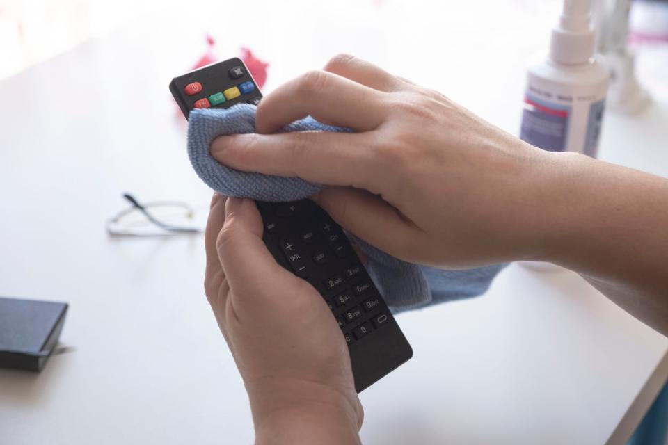 First-person perspective of cleaning a TV remote control with a microfiber towel