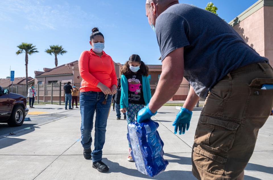 A mother and daughter wearing blue surgical masks are given a pack of Dasani waters, a bag of food and other perishable items during the League of United Latin American Citizens Salinas Council #2055 and United Farm Workers Foundation Food Distribution in Salinas, Calif, on Saturday, May 01, 2020.