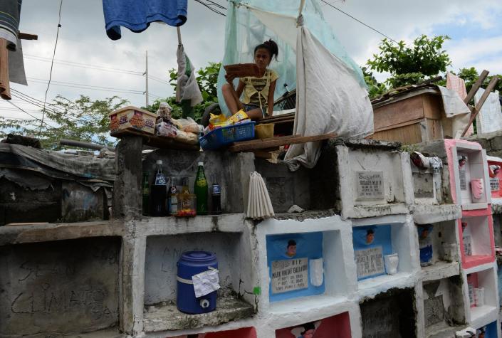 An temporary settler sells food to visitors from atop of the tombs at a cemetery in Manila, on October 31, 2014 (AFP Photo/Ted Aljibe)