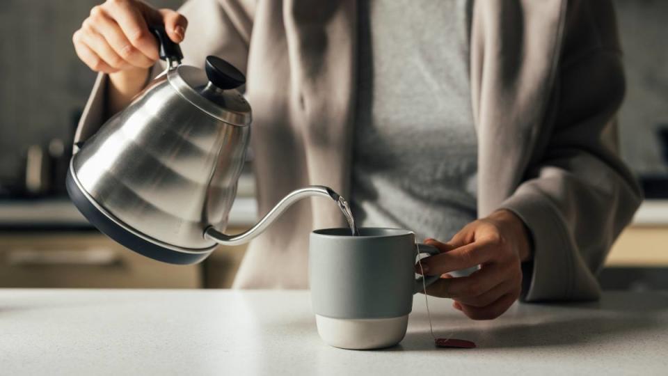 benefits of oregano tea: Hands of an unrecognizable woman pouring hot water into a cup to make a cup of tea.