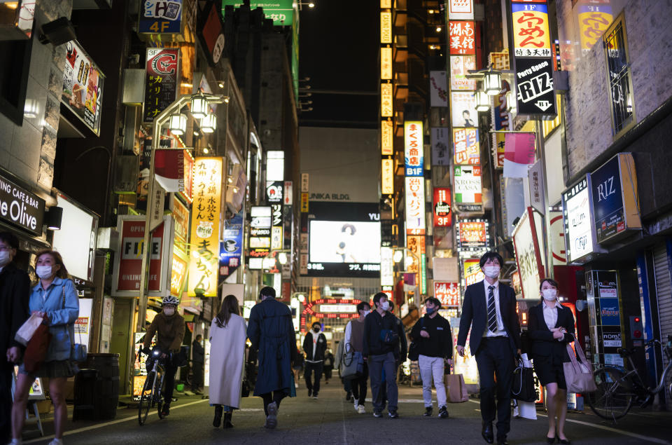 People walk through a street filled with entertainment, restaurants and bars in the Shinjuku neighborhood of Tokyo on Friday, April 9, 2021. Japan announced Friday that it will raise the coronavirus alert level in Tokyo to allow tougher measures to curb the rapid spread of a more contagious variant ahead of the Summer Olympics. (AP Photo/Hiro Komae)