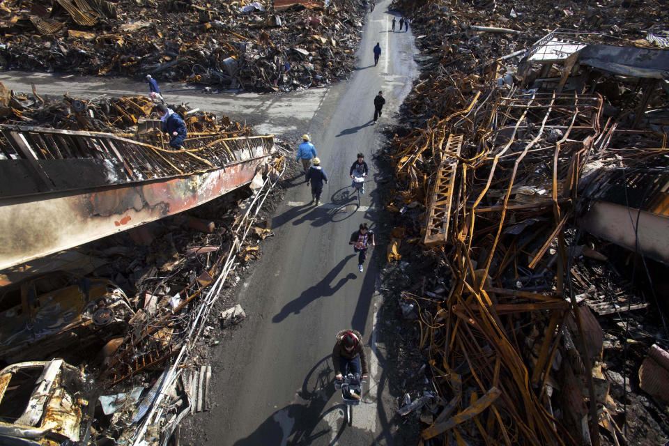 In this March 17, 2011, file photo, residents pass through a road that was cleared by bulldozer through the ruins of the city of Kesennuma, Miyagi Prefecture, northeastern Japan, six days after the March 11 tsunami. (AP Photo/David Guttenfelder, File)