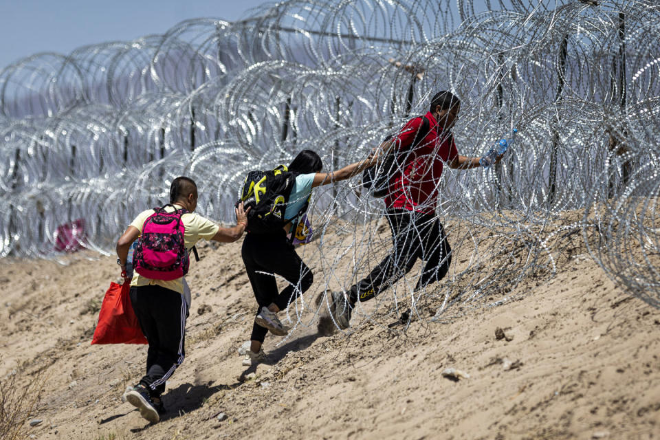 Immigrants walk through barbed wire around a makeshift migrant camp.  (John Moore/Getty Images)