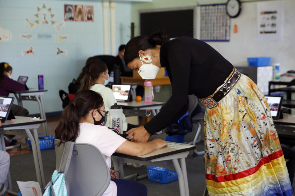 Multi-immersion teacher Randilynn Boucher-Giago assists a student during a lesson on boarding school history Sept. 29, 2021, in Pine Ridge, S.D. The lesson, Boucher-Giago says, aims to teach students about what many of their grandparents endured as well as their own resilience. (AP Photo/Emily Leshner)